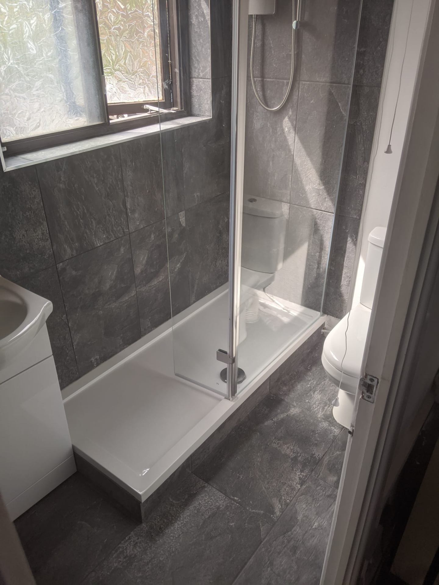 New walk-in shower with grey tiling and glass screen